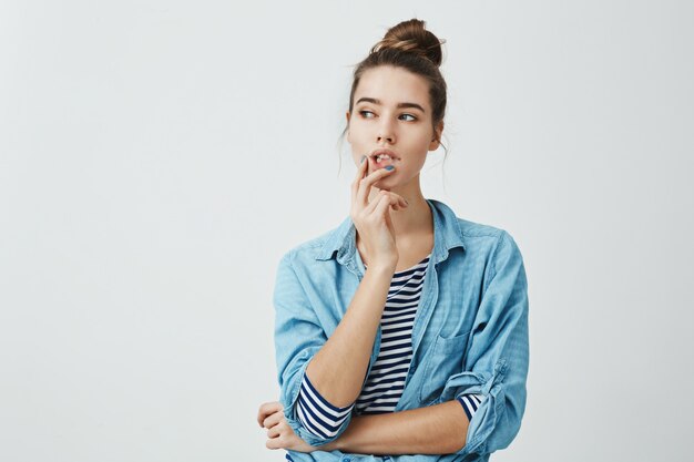 Fille faisant le plan quoi faire ensuite. Portrait de femme curieuse réfléchie avec coiffure chignon, tenant les doigts sur les lèvres tout en regardant de côté et en pensant à quelque chose qui la dérange