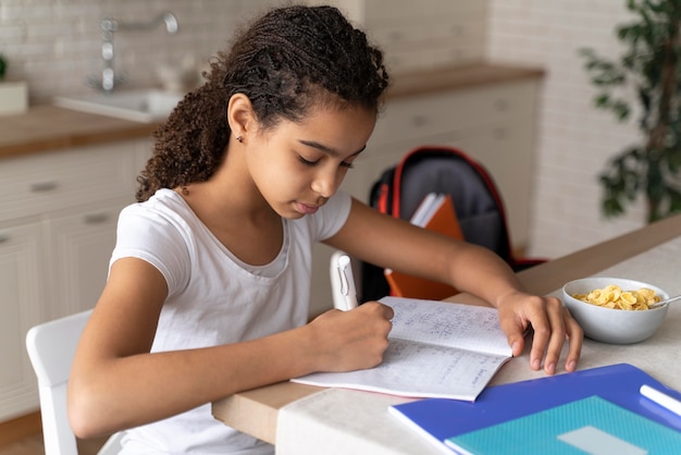 Fille faisant ses devoirs tout en prenant son petit déjeuner