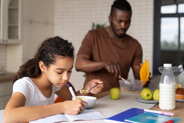 Fille faisant ses devoirs tout en prenant son petit déjeuner