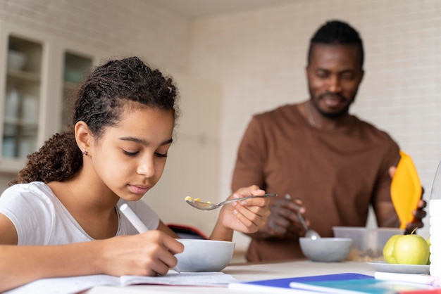 Fille faisant ses devoirs tout en prenant son petit déjeuner