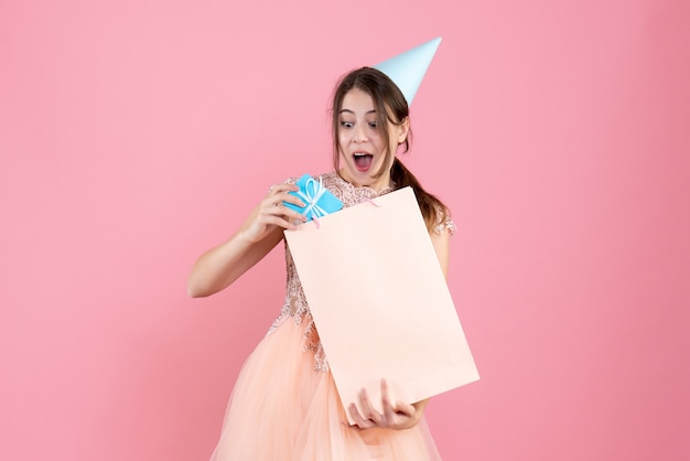 fille de fête avec chapeau de fête mettant un cadeau dans un sac rose