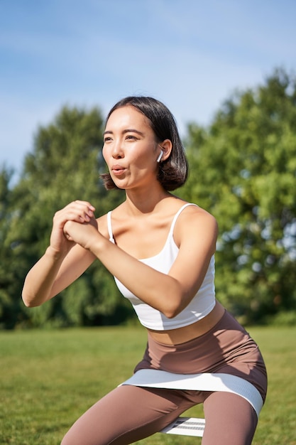 Fille De Fitness Asiatique Faisant Des Squats Dans Le Parc à L'aide D'une Bande De Résistance étirant La Corde De Yoga Pour Le Train D'entraînement