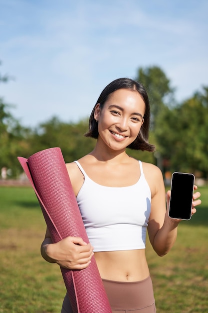 Une fille de fitness excitée recommande une application pour le sport et l'entraînement montre l'écran du téléphone debout avec r