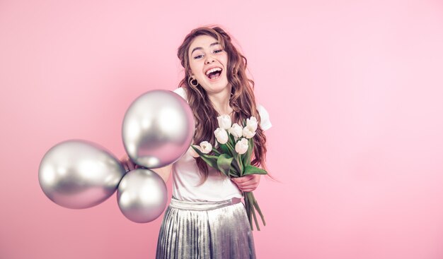 Photo gratuite fille avec des fleurs et des ballons sur un mur coloré