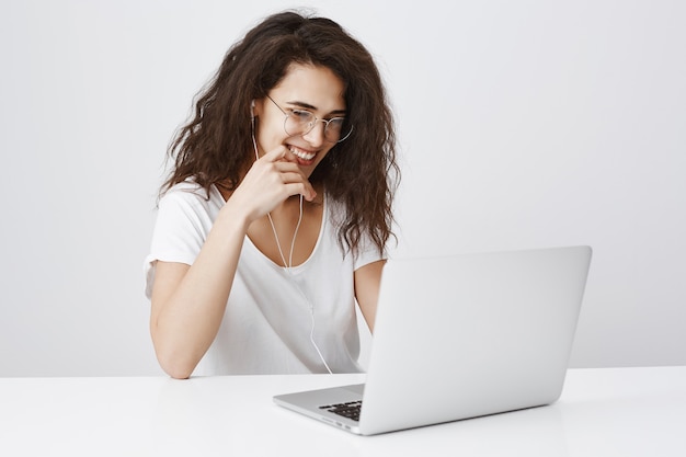 Fille gaie souriante dans les écouteurs, regardant un ordinateur portable et riant