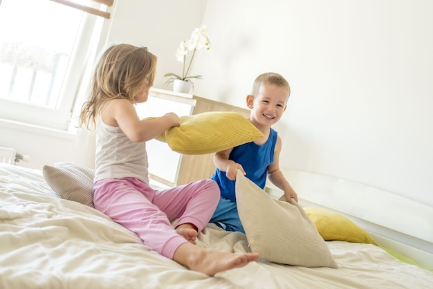 Fille et un garçon souriant et ayant une bataille d'oreillers sur un lit