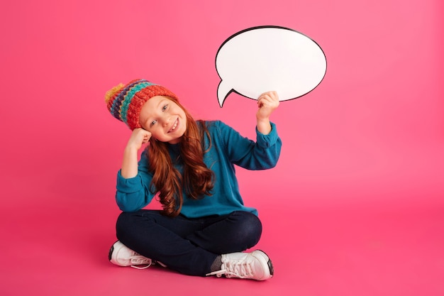 Fille de gingembre gai tenant le discours de bulle et regardant la caméra