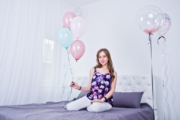 Fille heureuse avec des ballons colorés sur le lit dans la chambre Célébrer le thème de l'anniversaire