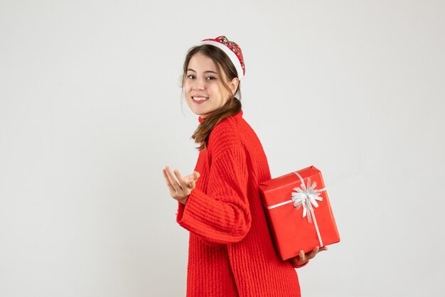 fille heureuse avec bonnet de Noel cachant son cadeau de Noël sur blanc
