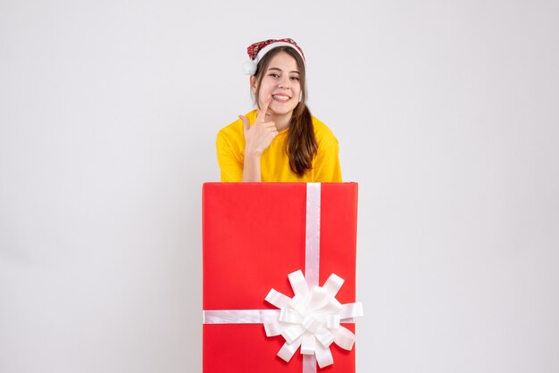 fille heureuse avec bonnet de noel montrant son sourire debout derrière un grand cadeau de Noël sur blanc