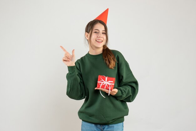 fille heureuse avec chapeau de fête pointant sur quelque chose sur blanc