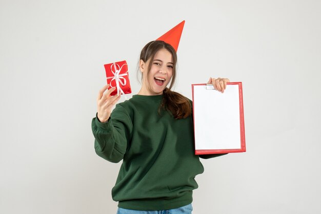 Fille heureuse avec chapeau de fête pointant sur son cadeau de Noël et document sur blanc