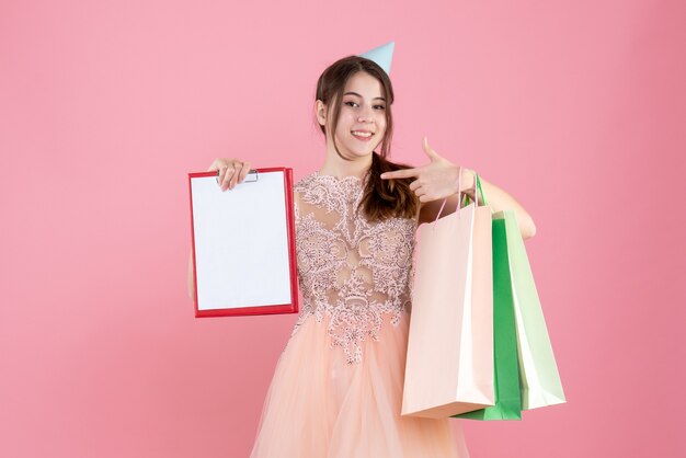 fille heureuse avec chapeau de fête tenant des documents et des sacs à provisions sur rose