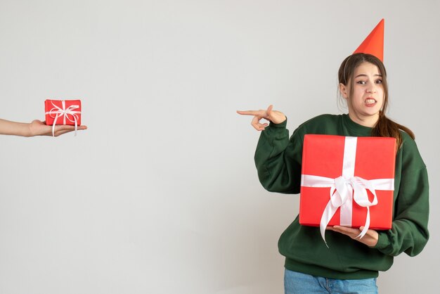 Fille heureuse avec chapeau de fête tenant son cadeau de Noël pointant sur la main de l'homme tenant un cadeau sur blanc