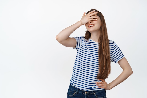 Fille heureuse con ses yeux avec la main et les sourires, jouant à cache-cache, attendant la surprise sur blanc