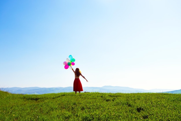 Fille heureuse dans les prés toscans avec des ballons colorés, contre le ciel bleu et le pré vert. toscane, italie
