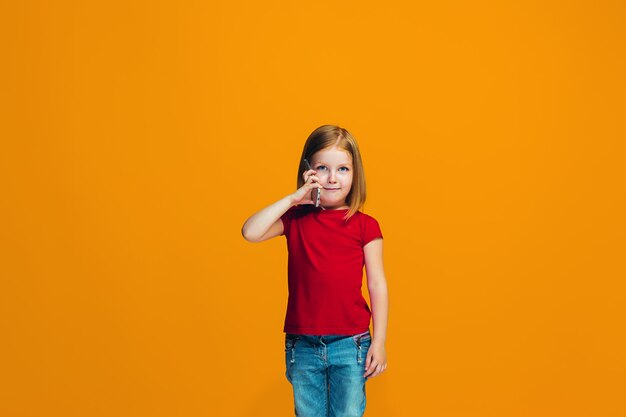 La fille heureuse debout et souriant contre le mur orange