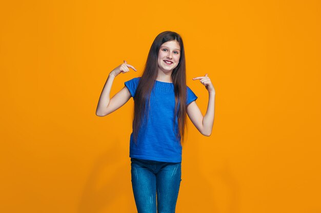 La fille heureuse debout et souriant contre le mur orange