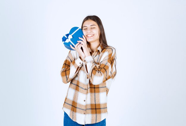 une fille heureuse embrasse un cadeau surprise sur un mur blanc.