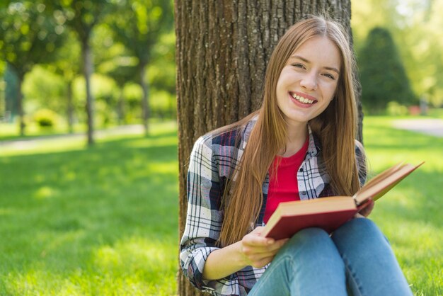 Fille heureuse, lisant un livre assis sur l'herbe