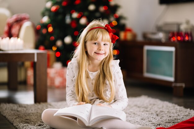 Fille heureuse avec livre en face de l&#39;arbre de Noël