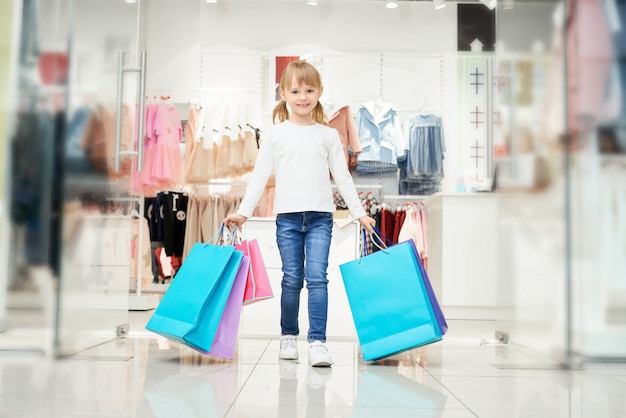 Fille heureuse avec de nombreux sacs colorés posant en magasin.