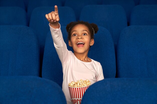 Fille heureuse pointant avec le doigt à l'écran et regarder un film