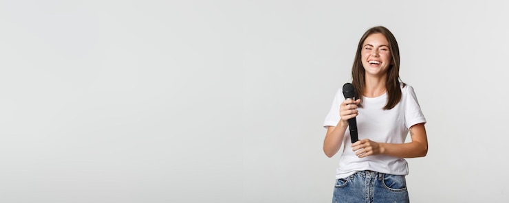 Photo gratuit une fille heureuse qui rit tenant un micro et chantant du karaoké sur un fond blanc