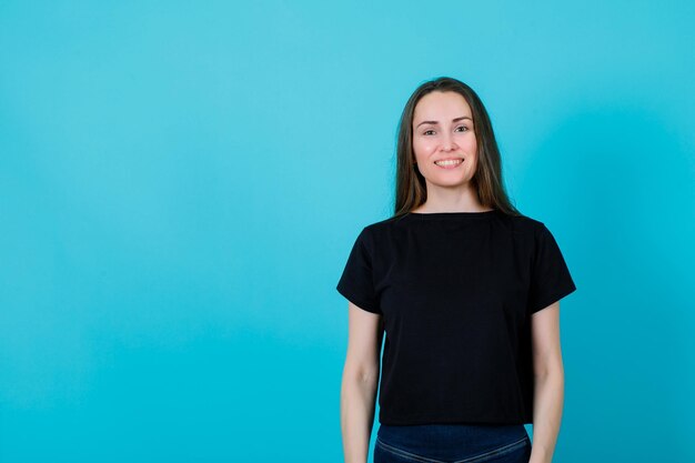 Une fille heureuse regarde la caméra en souriant sur fond bleu