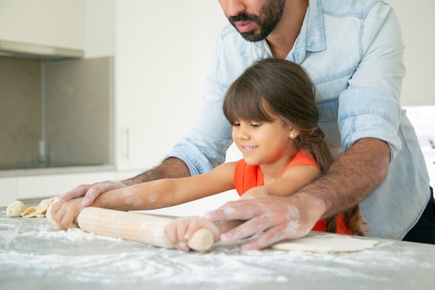 Fille heureuse et son père à rouler la pâte sur la table de cuisine avec de la farine en désordre.