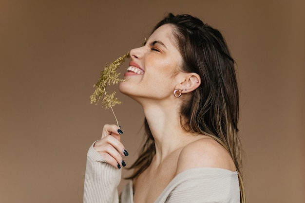 Fille heureuse tenant une fleur sur un mur marron. Dame attrayante souriante exprimant des émotions positives.