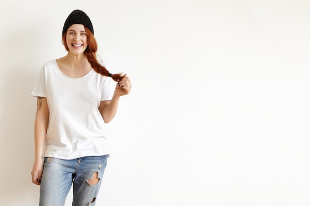 Fille de hipster portant un chapeau noir élégant, un t-shirt blanc et un jean en lambeaux souriant joyeusement