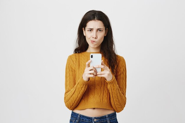 Une fille indécise reçoit un message frustrant, à la recherche d'un téléphone mobile hésitant