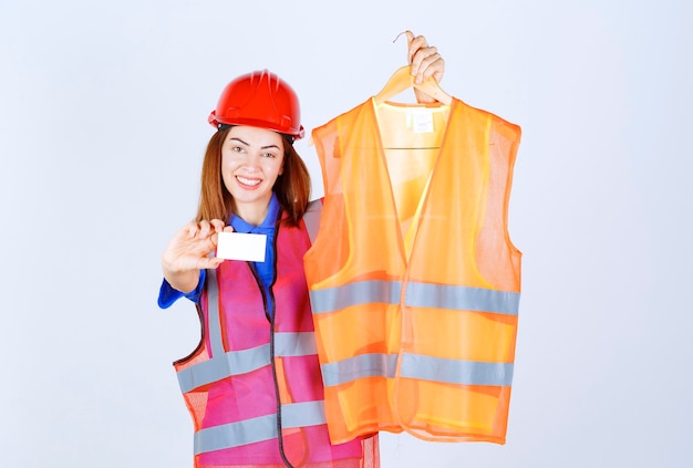 Fille ingénieur en uniforme présentant un morceau de veste de sécurité au collègue et présentant sa carte de visite.