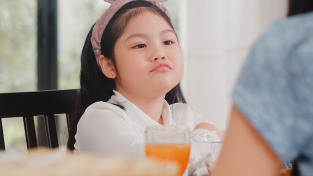 Fille japonaise asiatique s'ennuie avec de la nourriture. Les enfants de style de vie tristes n'aiment pas la nourriture contrarié le petit déjeuner dans la cuisine moderne à la maison le matin.