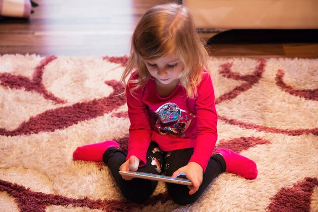 Fille jouant au jeu de tablette sur le sol