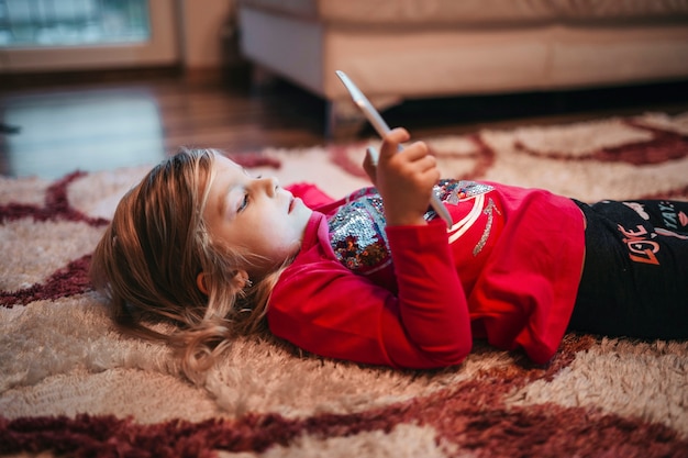 Photo gratuite fille jouant le jeu de la tablette sur le tapis