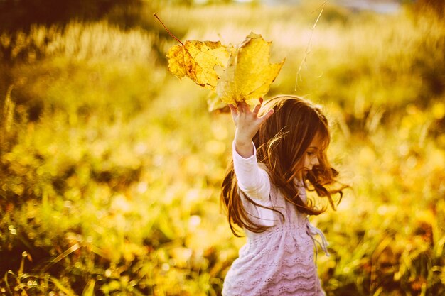 Fille joue avec des feuilles tombées dans la soirée