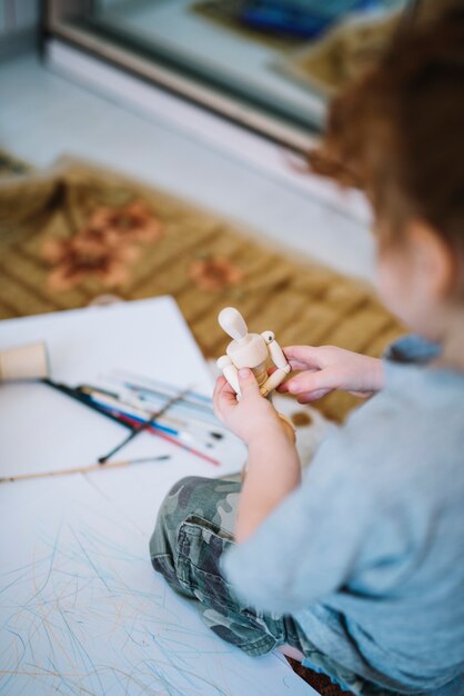 Fille avec jouet près de papiers et pinceaux et assis sur le sol