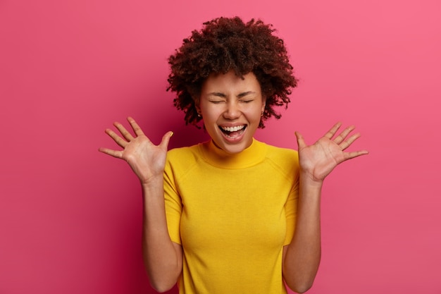 Fille Joyeuse Du Millénaire Joyeuse Rit Et Lève Les Paumes, A Une Expression De Visage Très Heureuse, Regarde Une Scène Drôle, Vêtue D'un T-shirt Jaune, Isolée Sur Un Mur Rose. Concept D'émotions Positives