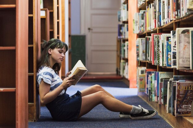 Fille de lecture assise sur le sol de la bibliothèque