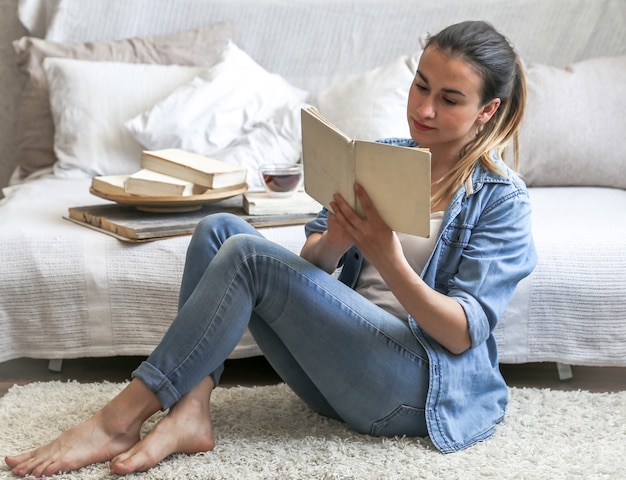 Fille lisant un livre dans une chambre confortable sur le canapé avec une tasse de thé, le concept de loisirs et de confort