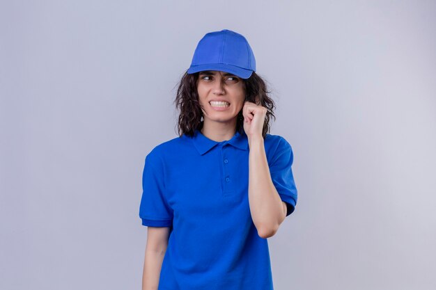 Fille de livraison en uniforme bleu et cap à confus et frustré debout sur un espace blanc isolé