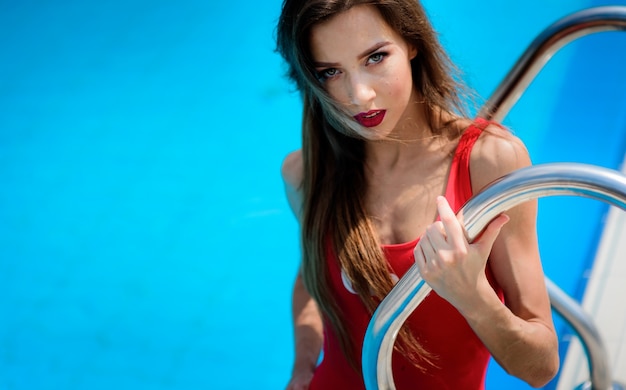 Une fille en maillot de bain rouge est assise près de la piscine bleue