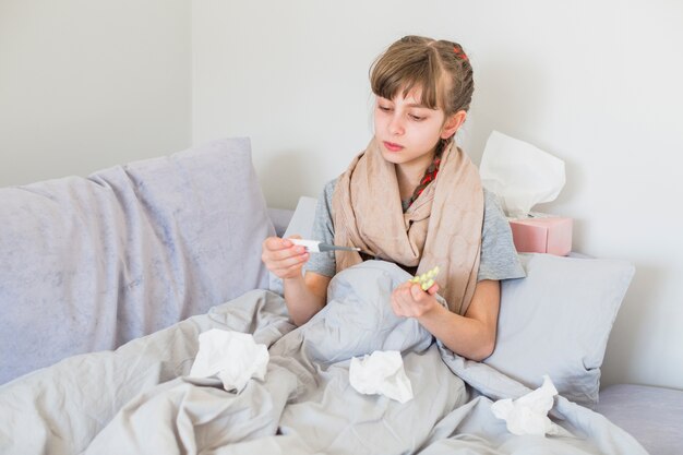 Fille malade utilisant un thermomètre