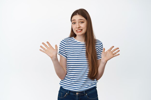 Fille maladroite haussant les épaules et montrant les mains vides levées rien à dire ne sais pas debout désemparé sur fond blanc