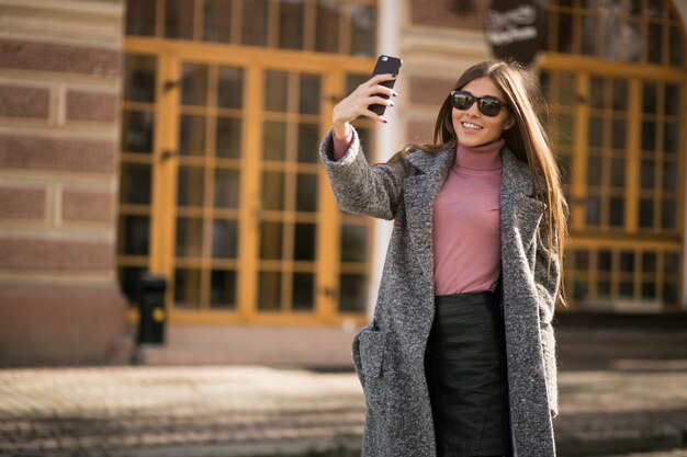 Fille en manteau avec téléphone debout dans la rue