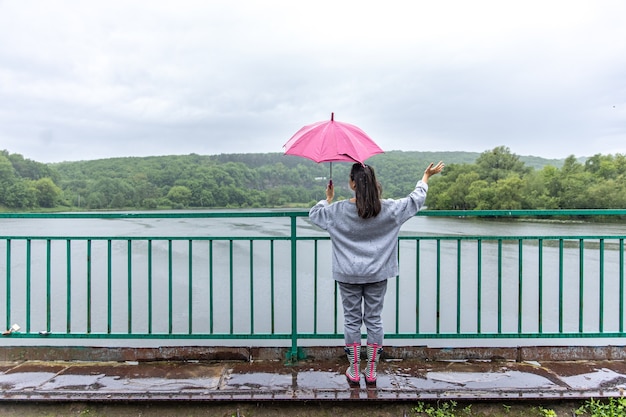 Photo gratuite une fille marche sous un parapluie par temps de pluie sur un pont dans la forêt.