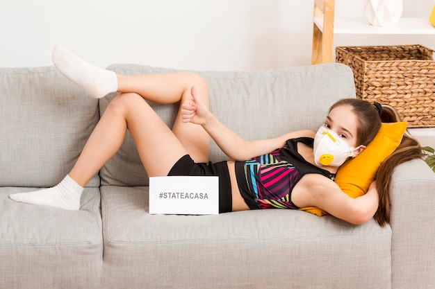 Fille avec masque assis sur le canapé