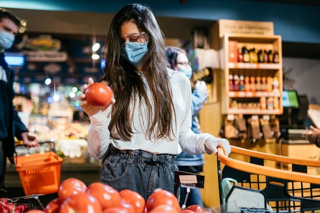 La fille avec un masque chirurgical va acheter des tomates.